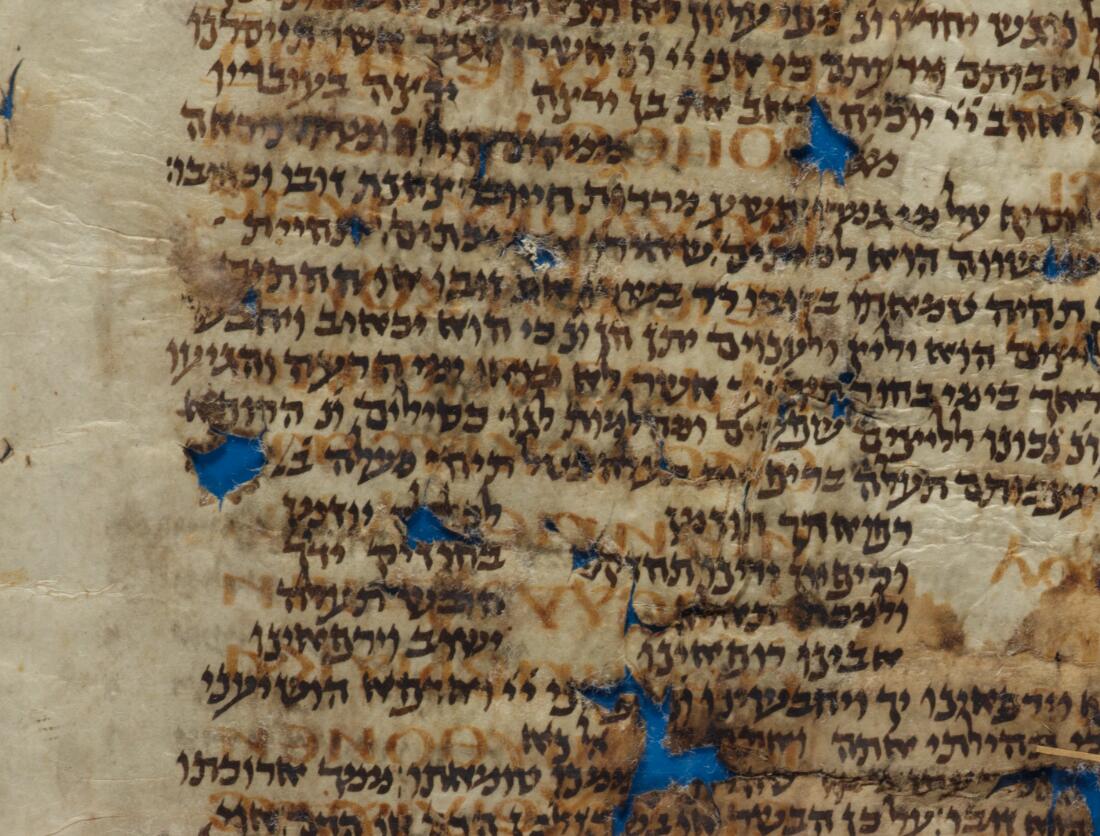 Close view of a densely written manuscript page with brown and red ink, showing tears and losses in the parchment.